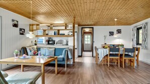 Ein geräumiger Wohnbereich mit Holzbalkendecke, einem Esstisch mit Stühlen, einer Couch und einer Küchenzeile mit Mikrowelle und weiteren Geräten.
