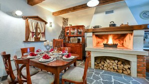 A dining area with a stone floor, wooden furniture, and a fireplace.