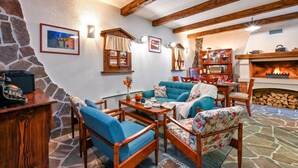 A cozy living room with a stone wall, wooden furniture, a fireplace, and a stone floor.