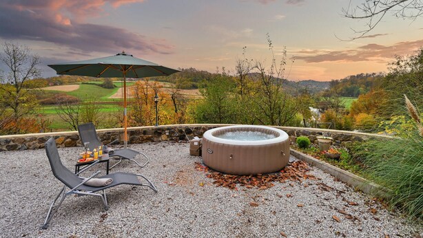 A hot tub with a stone wall backdrop, outdoor seating with a table and chairs, and a view of a golf course.