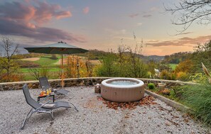 Un jacuzzi con un muro de piedra de fondo, mobiliario exterior con mesa y sillas, y vistas a un campo de golf.
