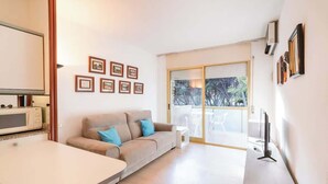 A modern living room with a sofa, a dining table, a TV, and a kitchen area with a microwave.