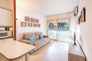 A modern living room with a sofa, a dining table, a TV, and a kitchen area with a microwave.