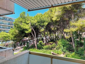 Un balcon donnant sur des arbres, avec un bâtiment visible au loin.