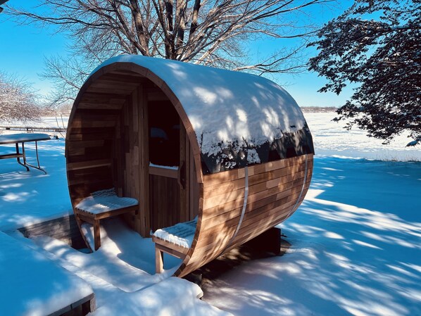A wooden barrel-shaped structure with a bench outside, surrounded by snow.