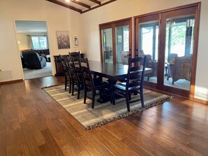 A dining area with a wooden table and chairs, a patterned rug, and a view through glass doors.