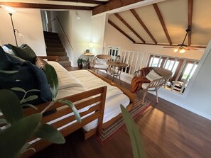A bedroom with a bed, a chair, a table, a lamp, and a staircase.
