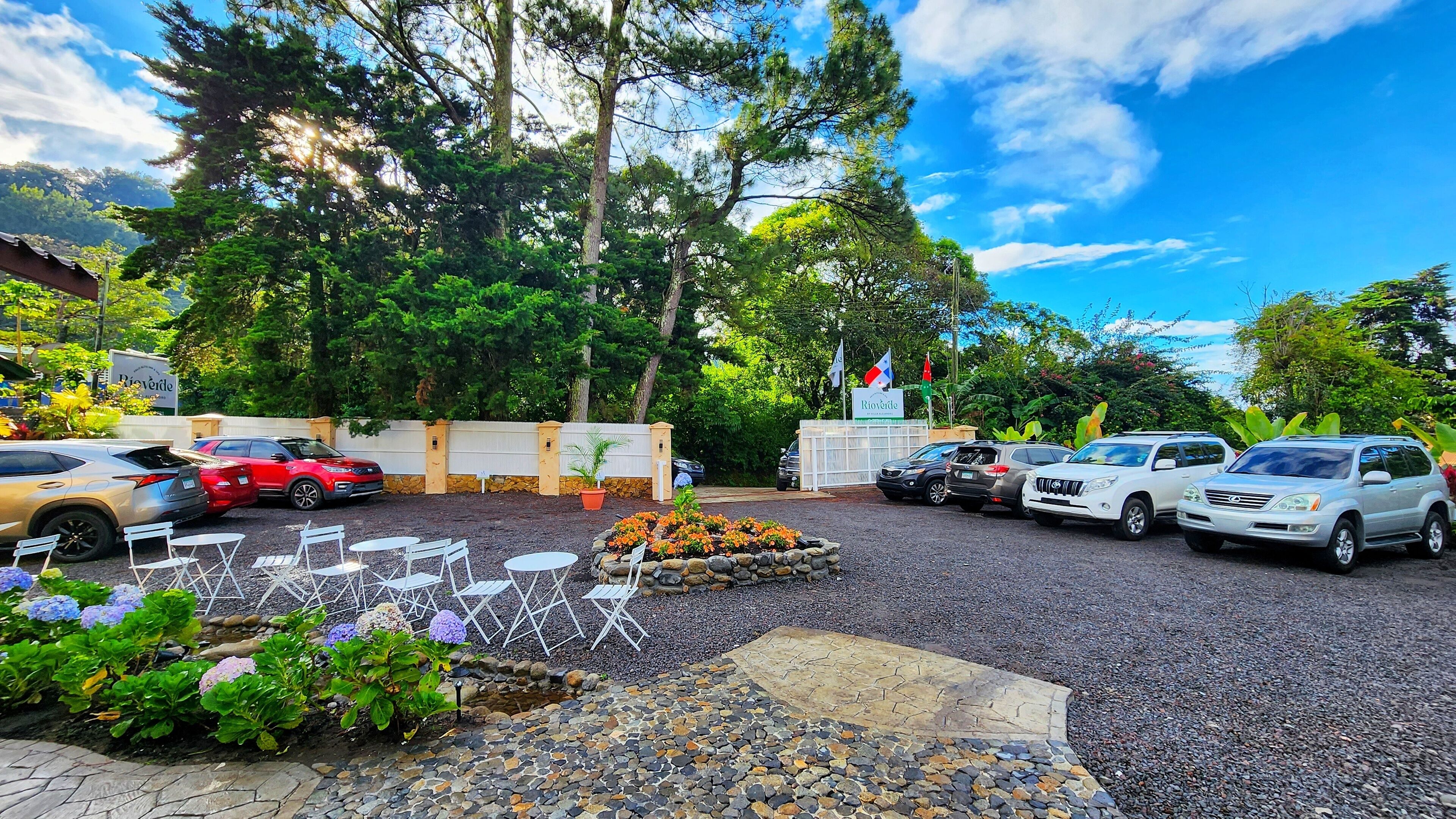 Un estacionamiento con varios coches, mobiliario exterior y un jardín con flores.
