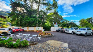 Un estacionamiento con varios coches, mobiliario exterior y un jardín con flores.