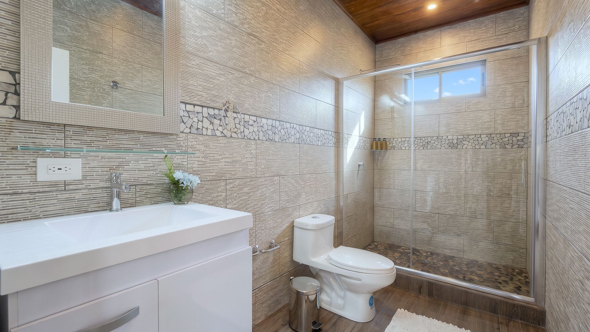 Un baño moderno con cabina de ducha de vidrio, un lavamanos blanco y un inodoro.