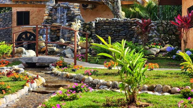 A garden with a stone bridge, a small waterfall, and various plants and flowers. - Rio Verde by Villa Alejandro (Los Naranjos)