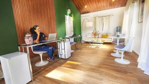 Una habitación moderna con techo de madera, pared de acento verde, sofá blanco, mesa de comedor con sillas y un ordenador portátil sobre una mesa de vidrio.