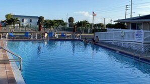 En swimmingpool med et hvidt hegn, liggestole og et flag.
