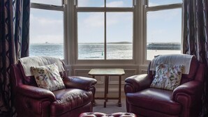 A room with two leather armchairs, a small table, and a matching ottoman. Large windows provide a view of the sea.