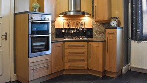 A compact kitchen with two ovens, a gas stove, wooden cabinets, and a tiled backsplash.