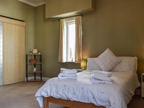 A neatly arranged bedroom with a bed, bedside tables, a shelf with decorative items, and a window with curtains. - 4 bedroom accommodation in Hartlepool (Hartlepool)