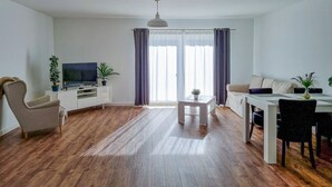 Ein Wohnzimmer mit Fernseher, einer Couch, einem Esstisch und Stühlen.