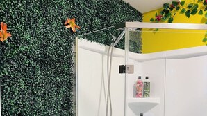 A shower with a green leafy wall, a white ceiling, and a yellow wall with a plant. - Talavera- vibrant Mexican-inspired apt in Salem (Salem)