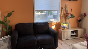 A living room with a black sofa, a wooden TV stand, and a window with blinds. - Talavera- vibrant Mexican-inspired apt in Salem (Salem)