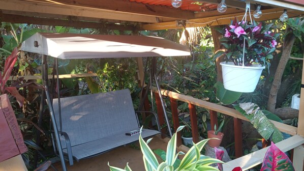 A covered outdoor seating area with a bench, a hanging planter, and various potted plants. - Smith House & Tropical Garden--Integrating Nature For Relaxation (Christiansted)