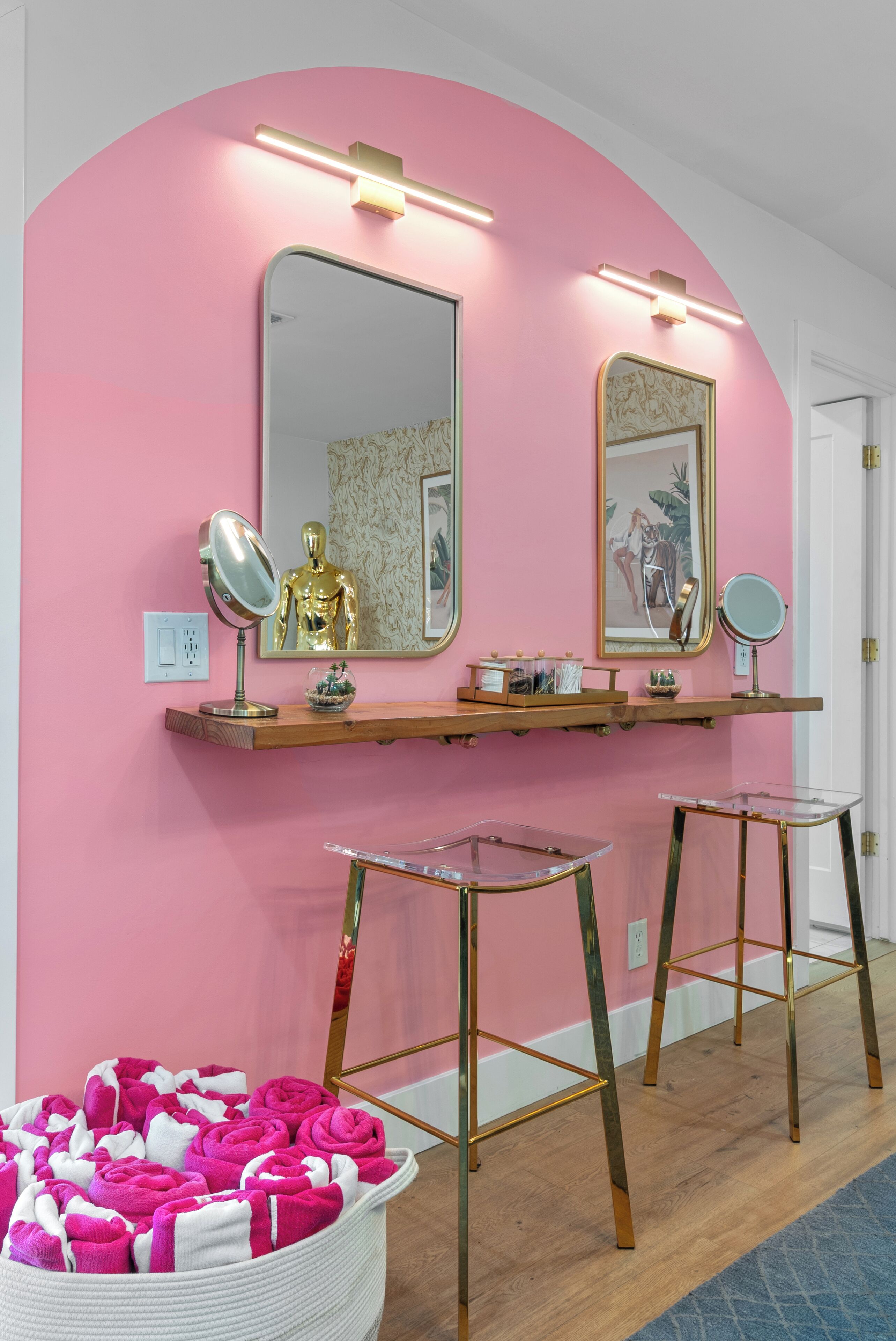 Un bagno con pareti rosa, un mobile vanitario con specchi e un portasciugamani bianco pieno di asciugamani.