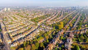 An aerial view of a residential area with rows of houses, roads, and a distant city skyline. - Lovely Studio Apartment in London (London)