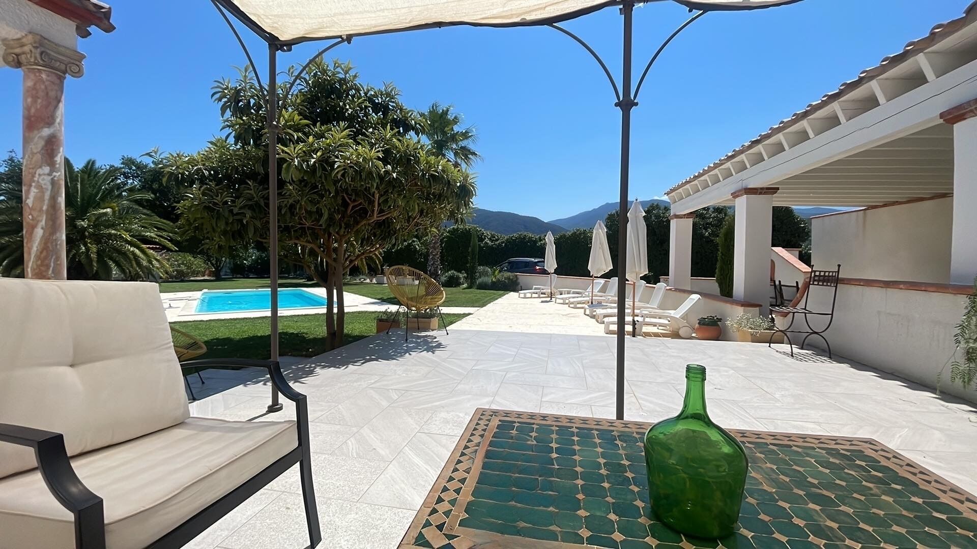 A patio with a pool, outdoor furniture, and a green bottle on a table.