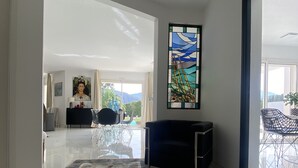 A spacious living area with a large window, a black sofa, a colorful rug, and a glass table. - Grande Villa Dans les Vergers de Pêchers (Bouleternère)