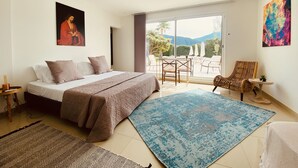 A bedroom with a bed, a large window, a balcony with chairs, and a painting on the wall. - Grande Villa Dans les Vergers de Pêchers (Bouleternère)