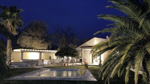 A well-lit outdoor area with a swimming pool, lounge chairs, and palm trees. - Grande Villa Dans les Vergers de Pêchers (Bouleternère)