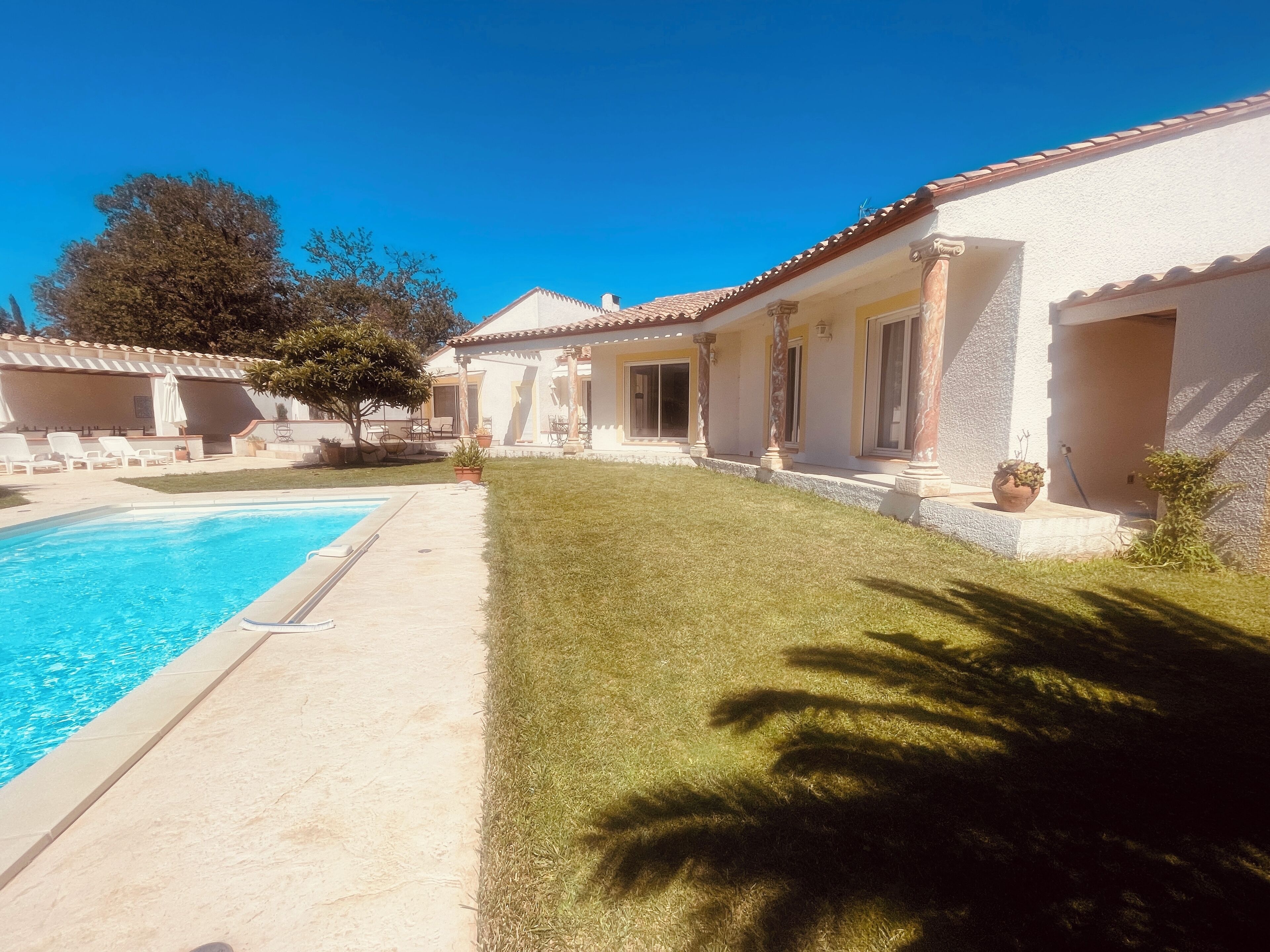 A poolside area with a clear blue pool, a well-maintained lawn, and a building with a tiled roof and columns.