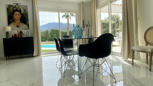 A modern dining area with a glass table, black chairs, and a view of a swimming pool and mountains. - Grande Villa Dans les Vergers de Pêchers (Bouleternère)