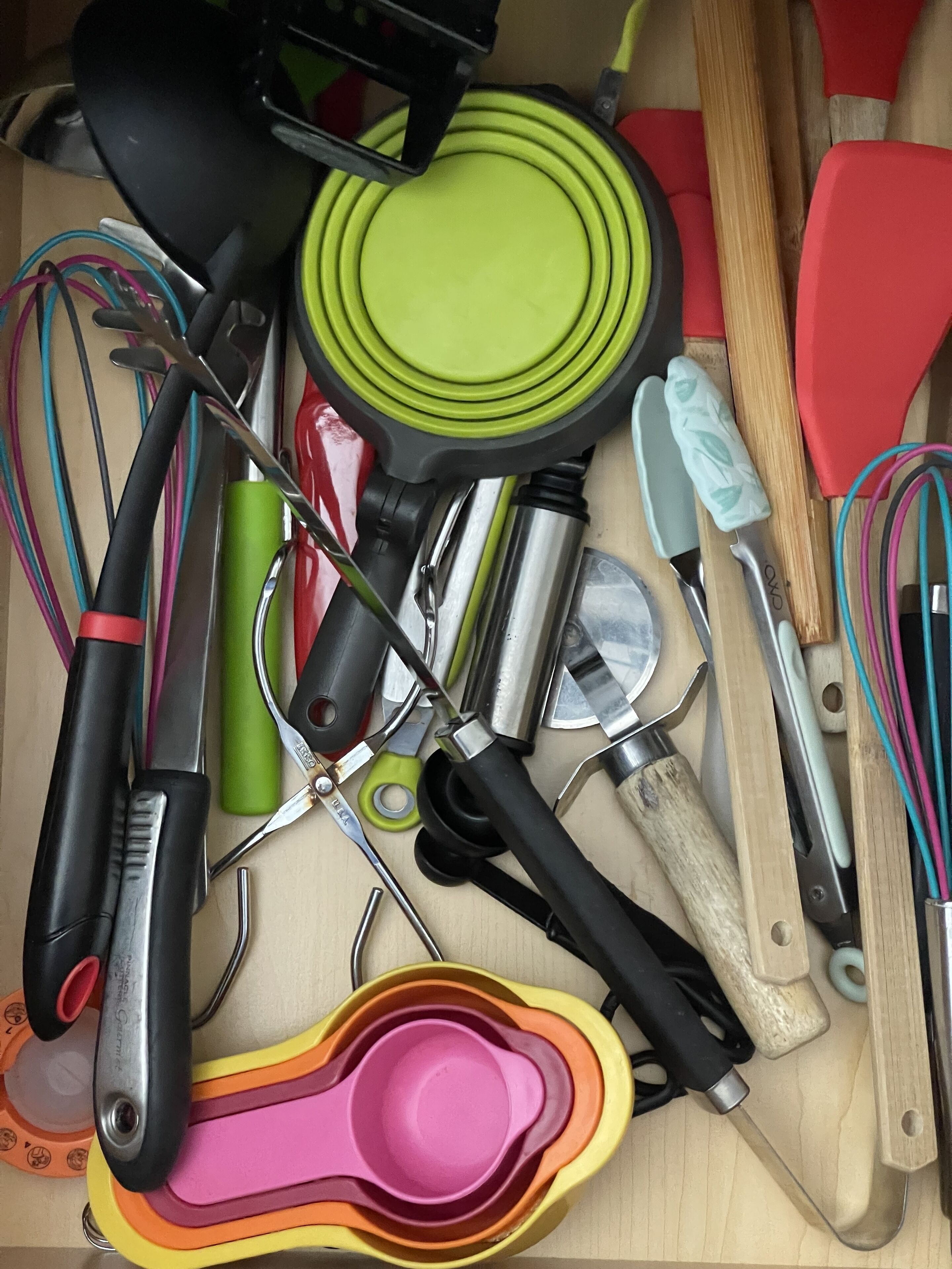 A drawer containing various kitchen utensils including whisks, a grater, and a set of measuring cups.
