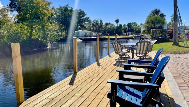 A wooden dock with chairs and a table, overlooking a calm body of water with a fountain. - EPIC Weeki Wachee riverfront home Waterfront Kayaks included (Spring Hill)