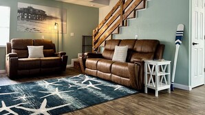 A living room with a brown leather sofa, a star-patterned rug, a wooden staircase, and a white door. - EPIC Weeki Wachee riverfront home Waterfront Kayaks included (Spring Hill)