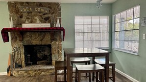 A room with a stone fireplace, a dining table with chairs, a window with blinds, and a wall-mounted sign. - EPIC Weeki Wachee riverfront home Waterfront Kayaks included (Spring Hill)