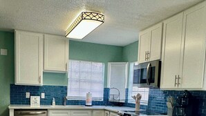 A modern kitchen with white cabinets, a central island with stools, a built-in microwave, and a dishwasher. - EPIC Weeki Wachee riverfront home Waterfront Kayaks included (Spring Hill)