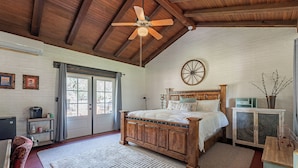 A bedroom with a wooden bed, a ceiling fan, a large window, and a rustic decor style. - Woodland Rd 1882 Historic 12-acre ranch, Resort landscape views up to 30 ppl (Tucson)
