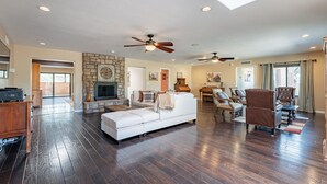 A spacious living room with a white sofa, a stone fireplace, and multiple ceiling fans. - Woodland Rd 1882 Historic 12-acre ranch, Resort landscape views up to 30 ppl (Tucson)