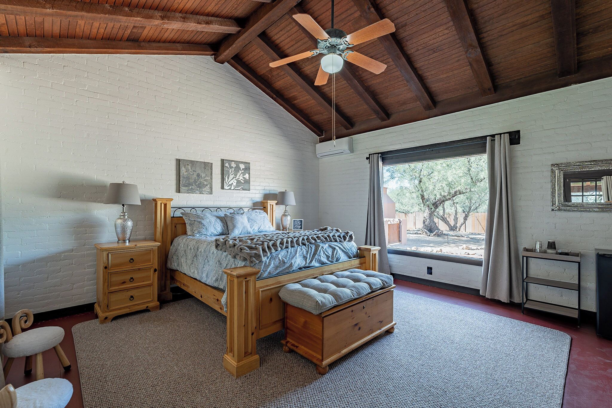 Une chambre à coucher avec un lit en bois, un ventilateur de plafond, une fenêtre avec des rideaux et une petite table de chevet avec une lampe.
