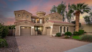 A two-story house with a stucco exterior, a large garage, and a landscaped front yard with a palm tree. - Heated pool, jacuzzi, Fast Wifi, Pac Man, Fire Pit, BBQ, Sleeps 14! (Phoenix)