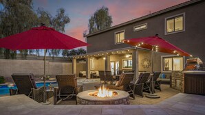 An outdoor patio with a fire pit, lounge chairs, and umbrellas. - Heated pool, jacuzzi, Fast Wifi, Pac Man, Fire Pit, BBQ, Sleeps 14! (Phoenix)