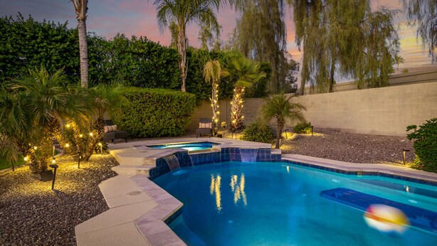 A swimming pool with a waterfall feature, surrounded by palm trees and a hedge. - Heated pool, jacuzzi, Fast Wifi, Pac Man, Fire Pit, BBQ, Sleeps 14! (Phoenix)