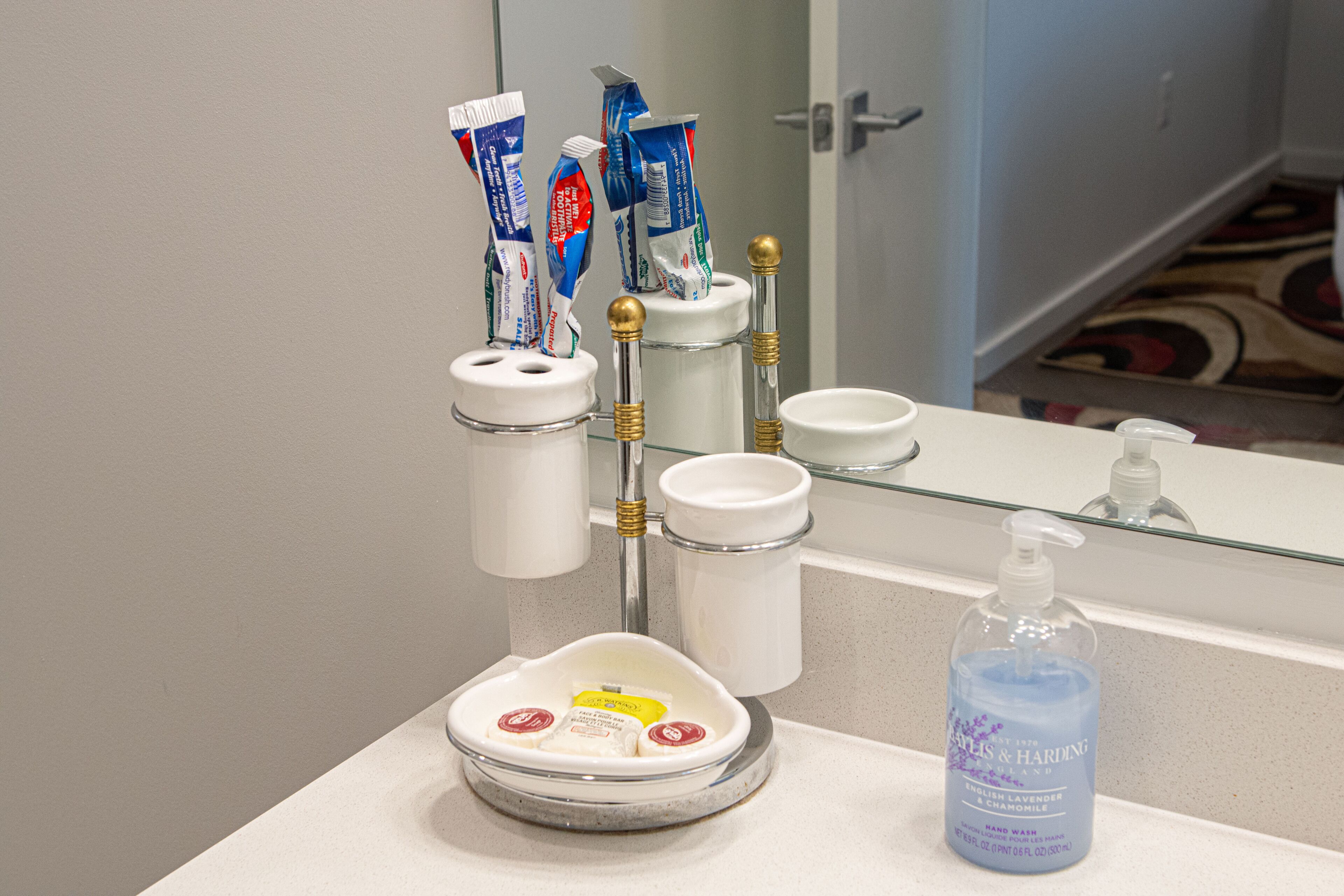 A bathroom sink with a toothbrush holder, a soap dish, and a hand soap bottle.