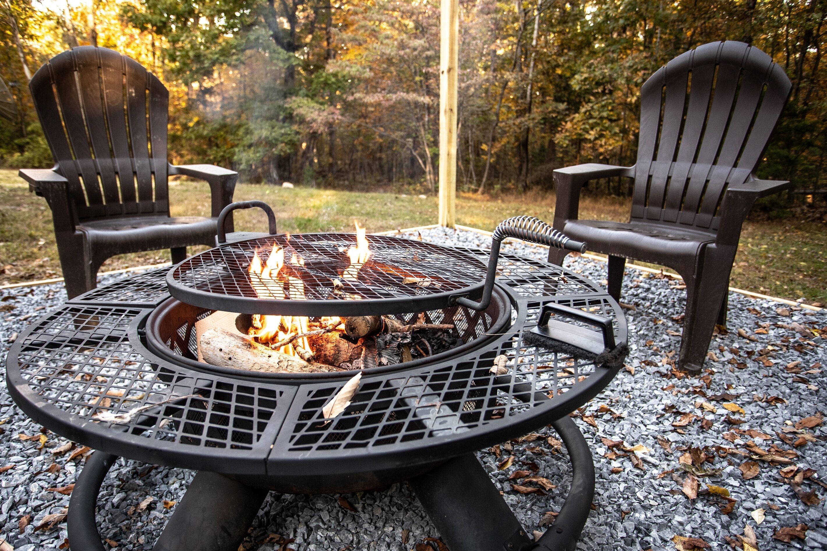 Una parrilla circular al aire libre con dos sillas, rodeada de grava y hojas de otoño.