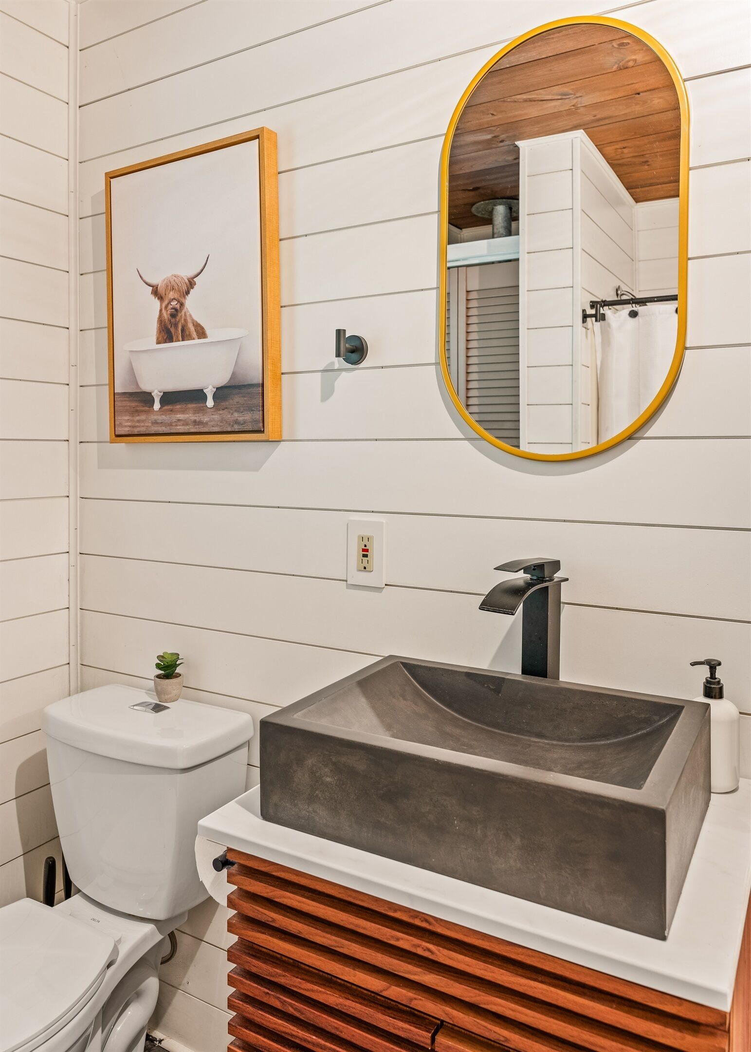 Un baño con tocador de madera, un lavamanos grande, un inodoro y un cuadro con una foto de un perro en una bañera.