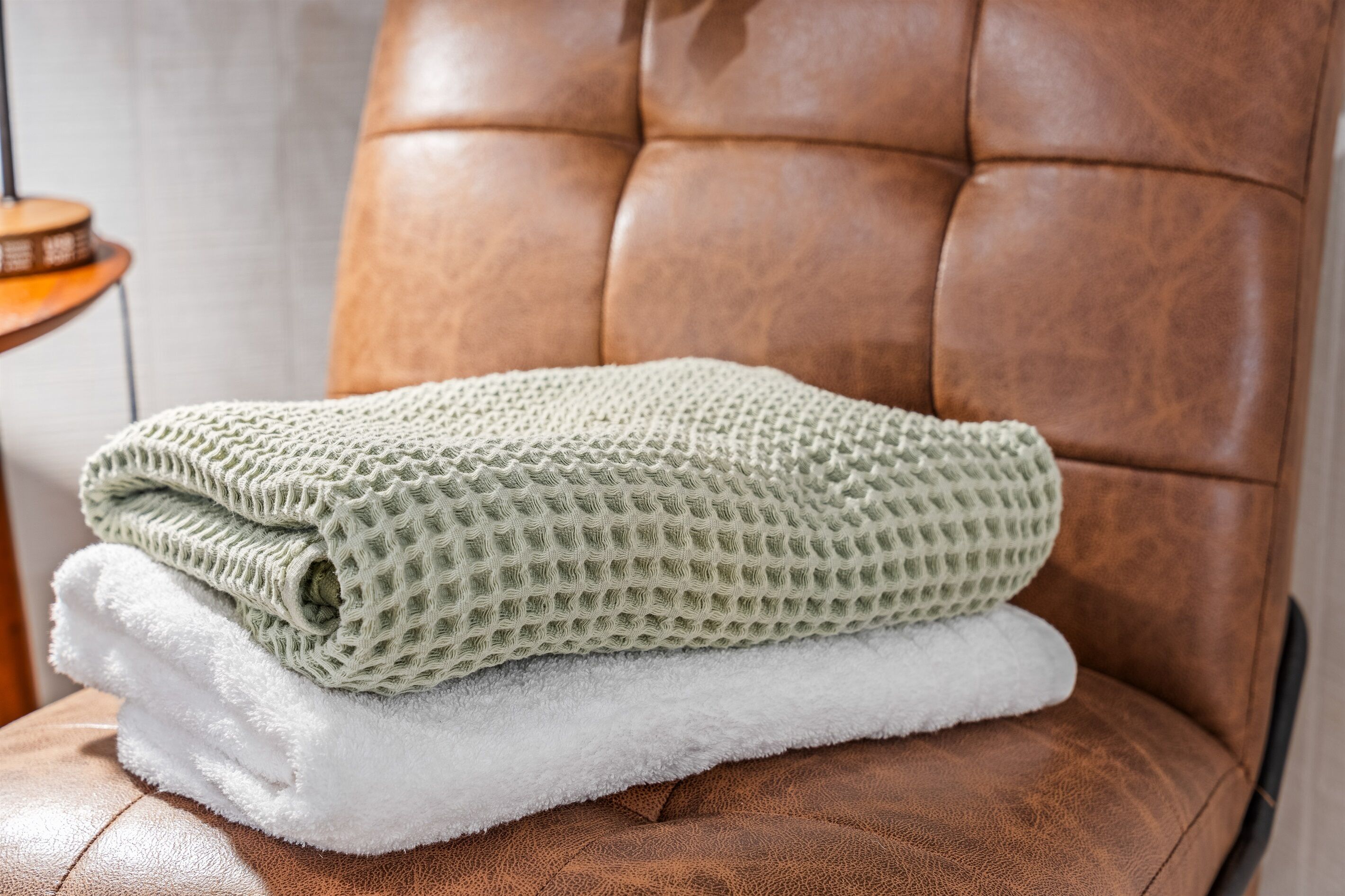 Una silla de cuero marrón con una manta verde y blanca texturizada doblada.