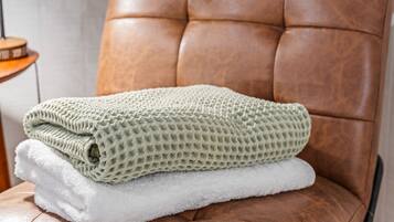 Una silla de cuero marrón con una manta verde y blanca texturizada doblada.