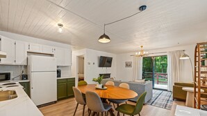 A modern kitchen with white cabinets, a wooden dining table, and a large window. - Outdoor Theatre | Hot Tub | Fire Pit | Dogs (Luray)