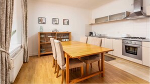 A compact kitchen with a wooden dining table, white cabinets, and a stainless steel range hood. - No27 The Barclay - Donnini Apartments (Kilmarnock)
